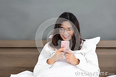 Oriental lady happily playing with mobile phone in bedroom Stock Photo