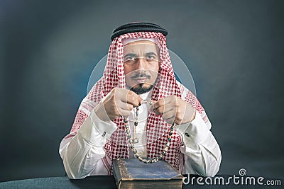 Oriental man in a white, traditional, national, Arabic dress dishdash, sitting with a rosary and the old Koran Stock Photo