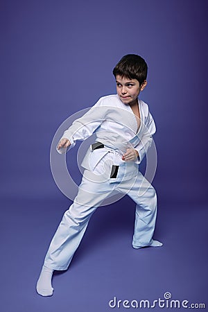 Oriental martial arts. Aikido fighter, Caucasian 10 years old boy in kimono improves his fighting skills, isolated on violet Stock Photo