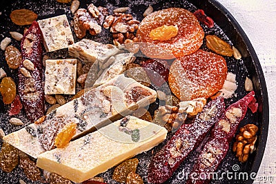 Oriental sweets - halva, dried apricots, raisins, walnuts, Churchchela, marmalade in powdered sugar on a black plate. Stock Photo