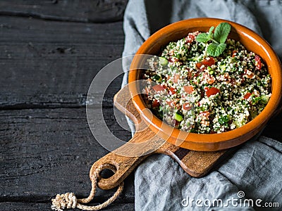 Oriental tabbouleh salad with couscous, vegetables and herbs in a brown bowl on a dark wood background Stock Photo