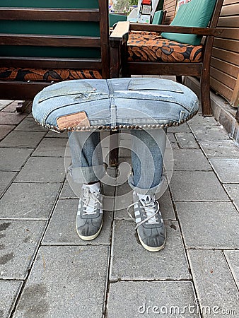 An original chair in the shape of legs. Creative sitting in nature - jeans and sneakers. Street stool next to the sidewalk. Turkey Editorial Stock Photo