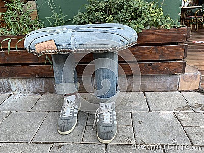 An original chair in the shape of legs. Creative sitting in nature - jeans and sneakers. Street stool next to the sidewalk. Turkey Editorial Stock Photo