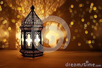 Ornamental Arabic lantern with burning candle glowing at night and glittering golden bokeh lights. Festive greeting card Stock Photo
