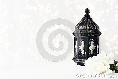 Ornamental dark Moroccan, Arabic lantern with peony flowers on white table and glittering bokeh lights. Greeting card Stock Photo