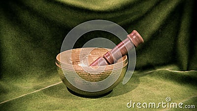 Ornate, hand-crafted Tibetan singing bowl stands against vibrant green cloth Stock Photo