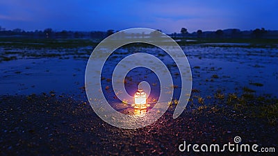 An ornate lantern glowing in the evening after sunset. On the ground, reflected in flood waters in a field on a winters evening. Stock Photo