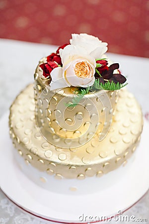 Ornate luxury golden polka dot festive wedding cake with flowers pink and red roses on top stands on white table Stock Photo