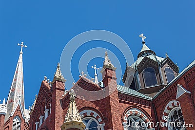 Ornate spires, domes, and windows of a Gothic Revival church featuring three white crosses against blue sky Stock Photo