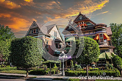 Ornate Victorian houses with gargole and colorful awnings and decorations and beautiful landscaping under pink and yellow sunset Stock Photo