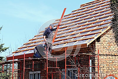Osiek, Poland - april 18, 2018: Two builders are hiding a roof on a brick house in the village. Construction work on a small facil Editorial Stock Photo