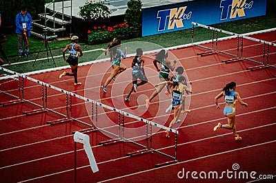Female Sprinters Competing in 100m Hurdles Race: Track and Field Athletes Navigate Obstacles for Editorial Stock Photo