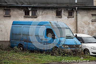 The abandoned wreck of a blue Mercedes-Benz Sprinter van overgrown by grass causing an environmental problem Editorial Stock Photo