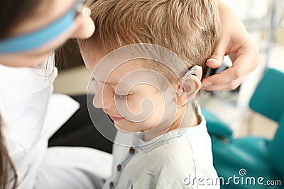 Otolaryngologist putting hearing aid in little boy's ear indoors Stock Photo
