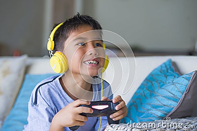 Oung hispanic little kid excited and happy playing video game online with headphones holding controller enjoying having fun sittin Stock Photo