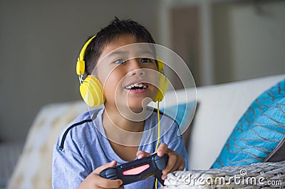 Oung hispanic little kid excited and happy playing video game online with headphones holding controller enjoying having fun sittin Stock Photo