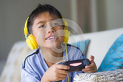 Oung hispanic little kid excited and happy playing video game online with headphones holding controller enjoying having fun sittin Stock Photo