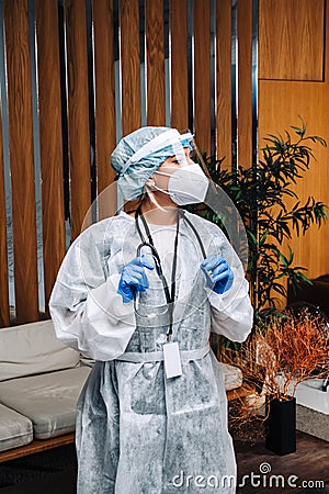 Oung woman nurse worker in medical protective mask, gloves and protective wear standing in hospital hall Stock Photo