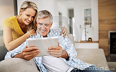 Our daughter finally e-mailed us her wedding album. a mature couple using a digital tablet while relaxing at home. Stock Photo