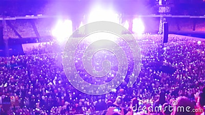 Out of focus image of big crowd of fans sitting on stadium seats watching and listening rock concert at night. Stock Photo