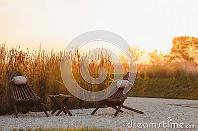 Outdoor al fresco chairs and table on a wooden deck at sunset in the spring with grape vines and hills in the background, Napa Stock Photo