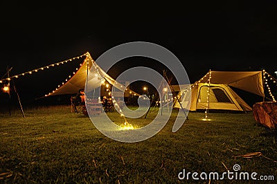 Outdoor camping tent with tarp or flysheet on grass courtyard and warm night light under dark night sky, family vacation picnic on Stock Photo