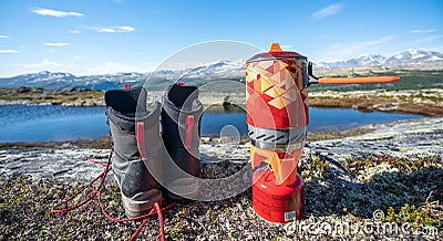 Outdoor cookery with propane gas boiler next to hiking boots with mountain scenery view. Stock Photo
