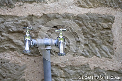 Outdoor double steel faucets in front of an old sandstone wall Stock Photo