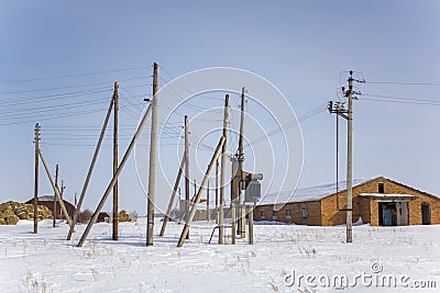 Outdoor electric transformer and a multitude of pillars with wires against a warehouse in winter Stock Photo