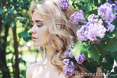 Outdoor fashion beautiful young woman surrounded by lilac flowers summer. Spring blossom lilac bush. Portrait of a girl blond Stock Photo