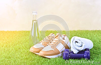 Outdoor fitness concept with sneakers footwear, dumbbells, bottle of water and towel on the green artificial grass. Stock Photo