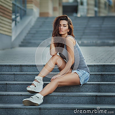 Outdoor lifestyle portrait of pretty young girl posing on stairway, wearing in hipster urban style on urban background Stock Photo