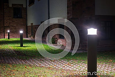 Outdoor lights in front of an old building illuminating a walkway in the garden at night Stock Photo