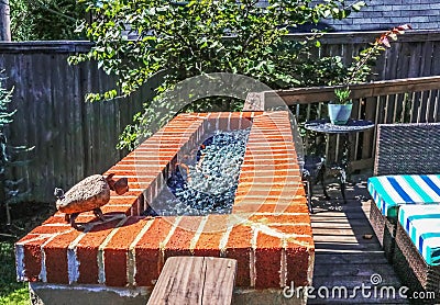 Outdoor natural gas fire pit with low flames on patio with privacy fence in background and colorful seating Stock Photo