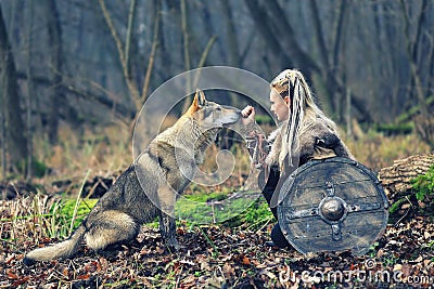 Outdoor northern warrior woman with braided hair and war makeup holding shield and ax with wolf next to her ready to attack - Stock Photo