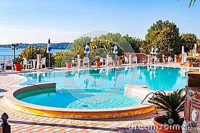 Outdoor pool with vibrant crystal water, parasols and deck chairs located on the coast of Garda lake in amazing La Ca camping in Editorial Stock Photo