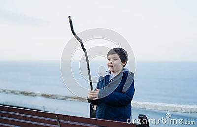 Outdoor portrait Active kid playing with wooden stick with blurry blue ocean seaside background, Happy boy having fun playing by Stock Photo