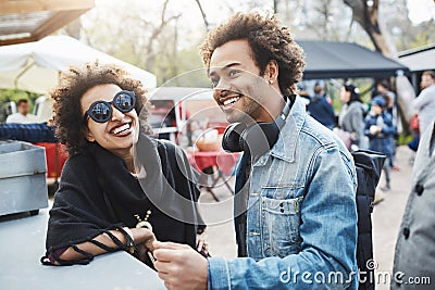 Outdoor portrait of happy african-american couple with afro hairstyles, leaning on table while on food festival Stock Photo