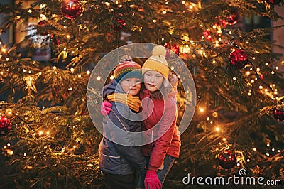 Outdoor portrait of little children next to Christmas tree with lights Stock Photo