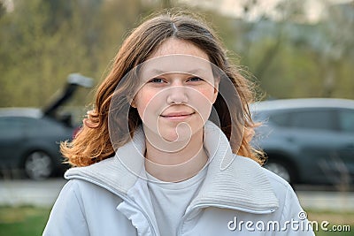 Outdoor portrait of teenager girl 15 years old, girl smiling with long brown hair in white jacket Stock Photo