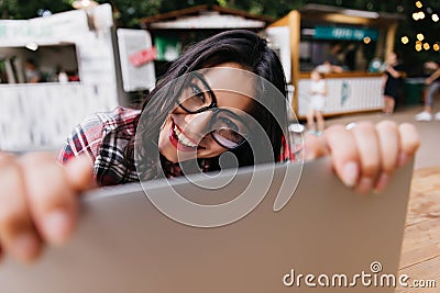 Outdoor shot of black-haired girl working with computer. Portrait of ecstatic tanned lady using lap Stock Photo