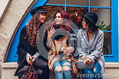 Outdoor shot of three young women chatting and laughing on city street. Best friends talking and having fun by cafe Stock Photo