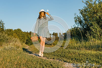 Outdoor summer portrait of girl teenager walking in rural country road in dress and hat with basket of strawberries. Nature Stock Photo