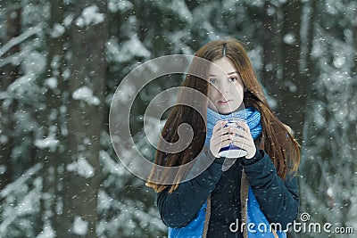 Outdoor winter portrait of freezing young lady holding cup with hot drink during heavy snowfall in conifer forest Stock Photo