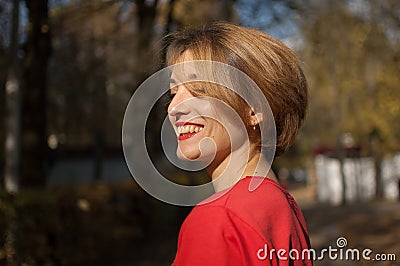 Outdoors female portrait of attractive young woman with charming smile, blond short hair, sensual lips, and red clothes Stock Photo