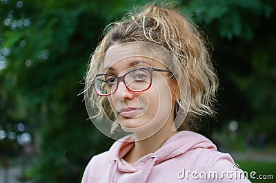 Outdoors female portrait of young girl with blonde hair in pink sweater wearing hipster eyeglasses in the park Stock Photo