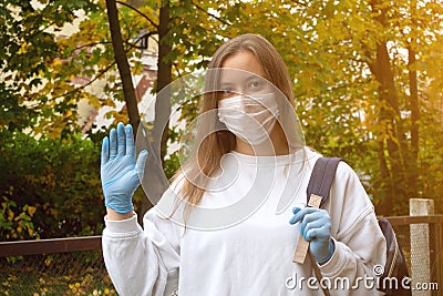 Outdoors portrait of beautiful young woman wearing cotton white mask and medicalgloves greeting and say hello, Nature and trees in Stock Photo