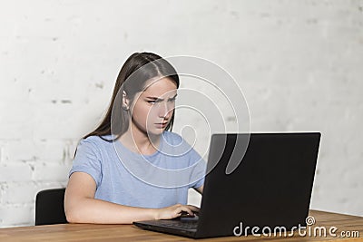 Outraged girl typing on a laptop, sitting at the table Stock Photo