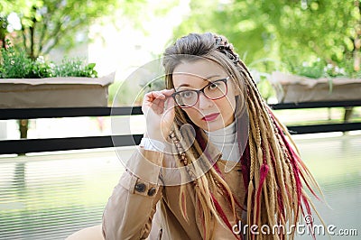 Outside portrait of young independent woman in eyeglasses, casual nude trench with long dreadlocks sitting in outdoor Stock Photo