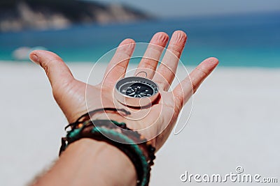 Outstretched hand holding black metal compass against white sandy beach and blue sea. Find your way or goal concept Stock Photo